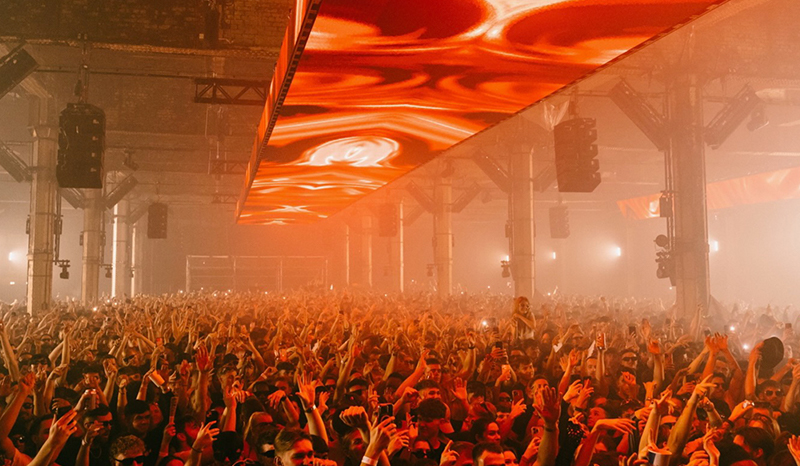 Crowd with hands up under a glowing orange ceiling screen