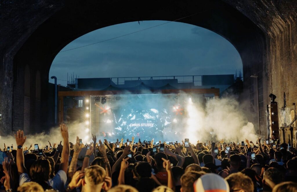 Crowd under a railway arch with a smoky stage